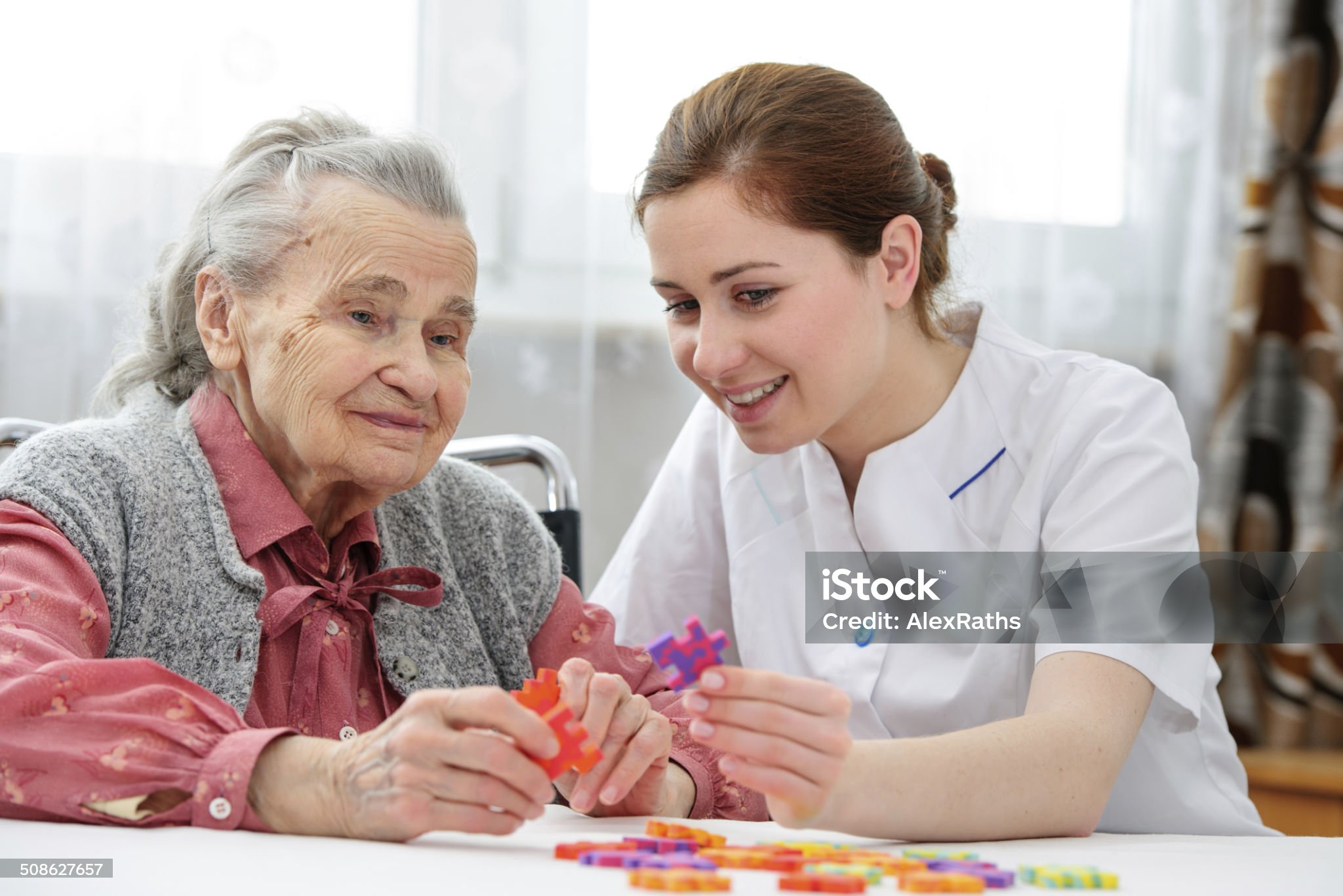 Elder care nurse playing jigsaw puzzle with senior woman in nursing home Pflegedienst Köln Herzblick
